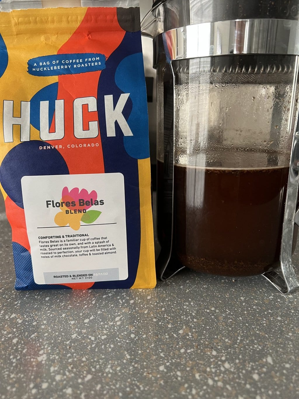 a pack of Huck Coffee next to a French press in which coffee is brewed